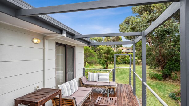 A covered outdoor seating area with a wooden deck, a sofa, and a table. - Three Beaches (Anglesea)