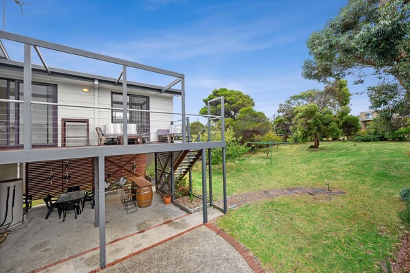 A modern two-story house with a covered outdoor seating area, a staircase, and a well-maintained lawn.
