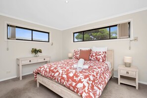 A bedroom with a large bed, two bedside tables, a nightstand, a window with a view, and a wall-mounted light fixture. - Three Beaches (Anglesea)