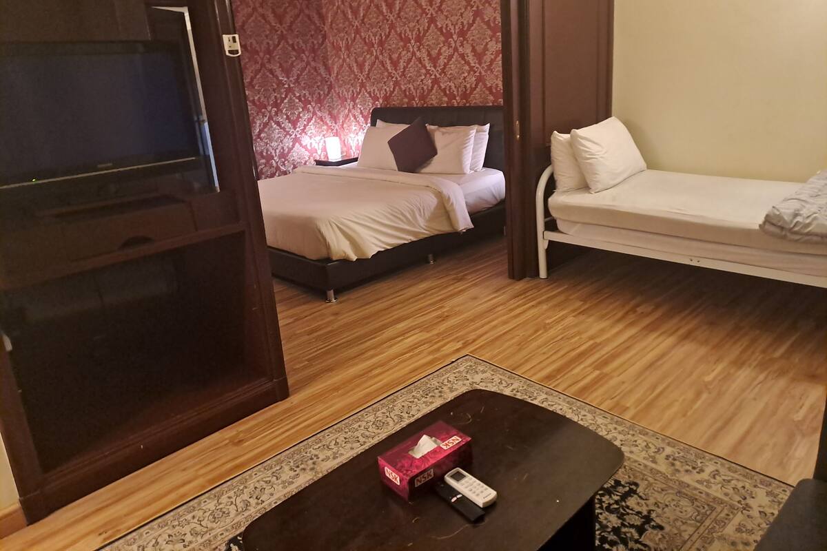 A hotel room with a bed, a sofa, a small table with a tissue box, and a patterned rug.