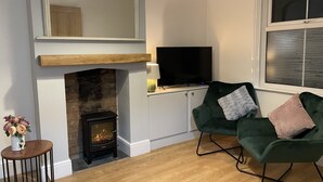 A cozy living room with a fireplace, a television, and a green armchair. - Beautiful Townhouse in Stratford Upon Avon (Stratford-upon-Avon)