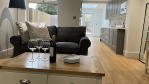 A modern kitchen with grey cabinets, a wooden countertop, and a black sofa with cushions. There are wine glasses and a bottle on the countertop. - Beautiful Townhouse in Stratford Upon Avon (Stratford-upon-Avon)