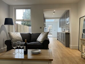 Una cocina moderna con armarios oscuros, encimera de madera y un rincón comedor con sofá negro y una mesa servida con copas de vino y platos.
