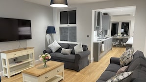 A modern living room with a grey sofa, a wooden coffee table, and a TV. - Beautiful Townhouse in Stratford Upon Avon (Stratford-upon-Avon)