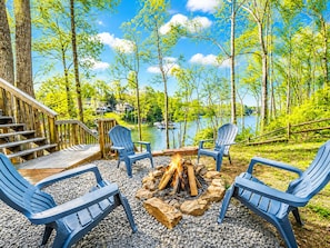 A deck with Adirondack chairs, a fire pit, and a lake view.