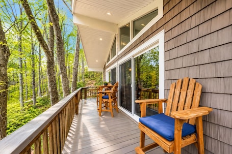 A wooden deck with a table and chairs, overlooking a forest.. Treetop & Waterfront! Quiet Cove, Hot Tub, Kayaks, Game Room and more