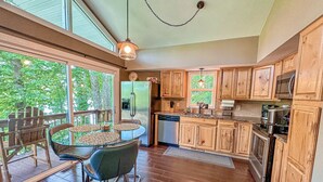 A kitchen with wooden cabinets, a stainless steel refrigerator, a dishwasher, and a dining area with a glass table and chairs. - Treetop & Waterfront! Quiet Cove, Hot Tub, Kayaks, Game Room and more (Moneta)
