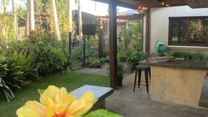 Un espace extérieur abrité doté d’un sol en béton, d’une pergola en bois et d’un petit comptoir de bar.