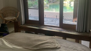 Une chambre d’hôtel avec un lit, une fenêtre donnant sur une piscine et un espace verdoyant, et un fauteuil en osier.