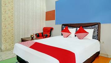 A hotel room with a large bed, a red and white bedspread, two red pillows, a red chair, and a blue accent wall.