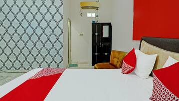 A hotel room with a bed, a red and white patterned wall, a red and white pillow, and a brown chair.