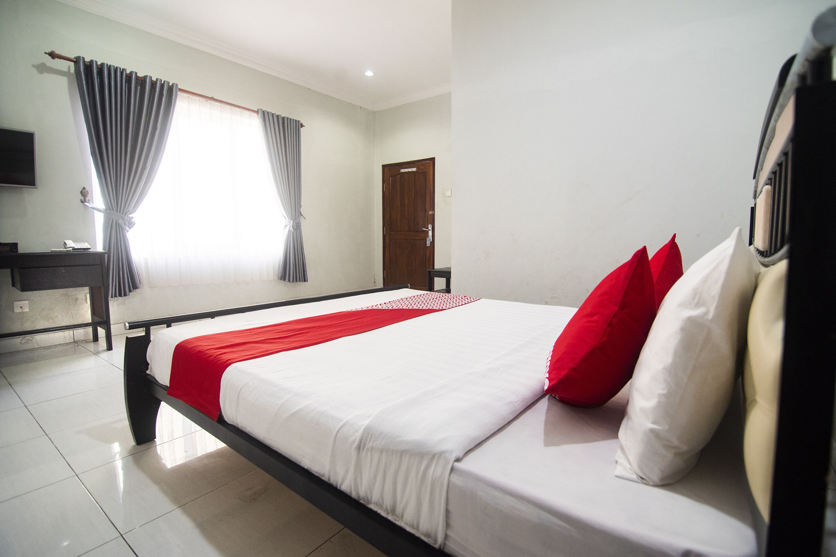 A hotel room with a bed, a desk, a chair, a TV, and a door.