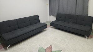 A room with two dark sofas, a patterned rug, and a window with grey curtains. - Jipu Homestay (Betong)