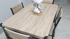 A dining table with a wooden top and black metal legs, surrounded by four chairs with wooden backs and black metal armrests. - Jipu Homestay (Betong)