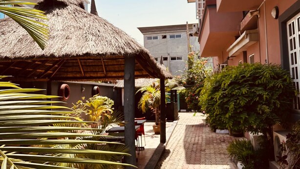 A courtyard with a thatched-roof structure, potted plants, and a paved walkway. - BATES GARDEN GUEST HOUSE (Lekki)