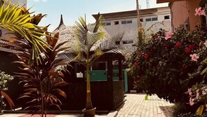 A paved pathway with potted plants and flowers, leading to a building with a thatched roof structure. - BATES GARDEN GUEST HOUSE (Lekki)