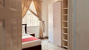 A bedroom with a bed, a wardrobe, and a window with curtains. - BATES GARDEN GUEST HOUSE (Lekki)