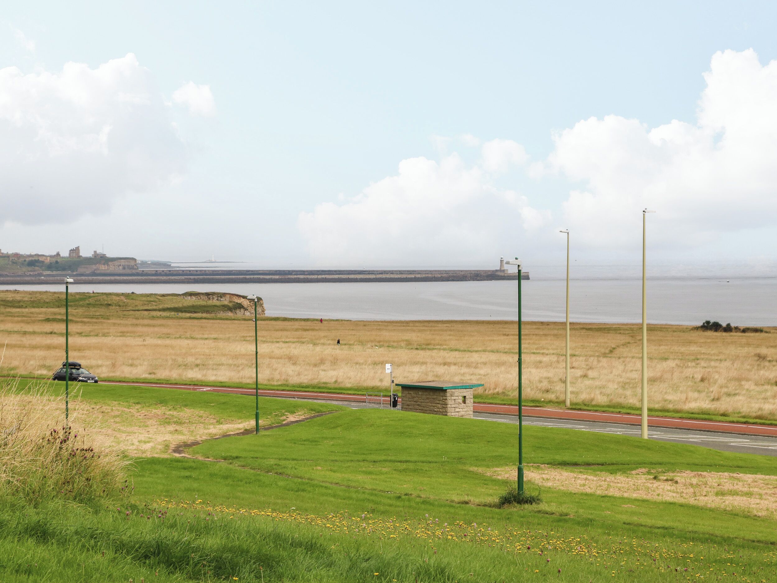 Uma estrada costeira com área gramada e uma vista distante de um farol.