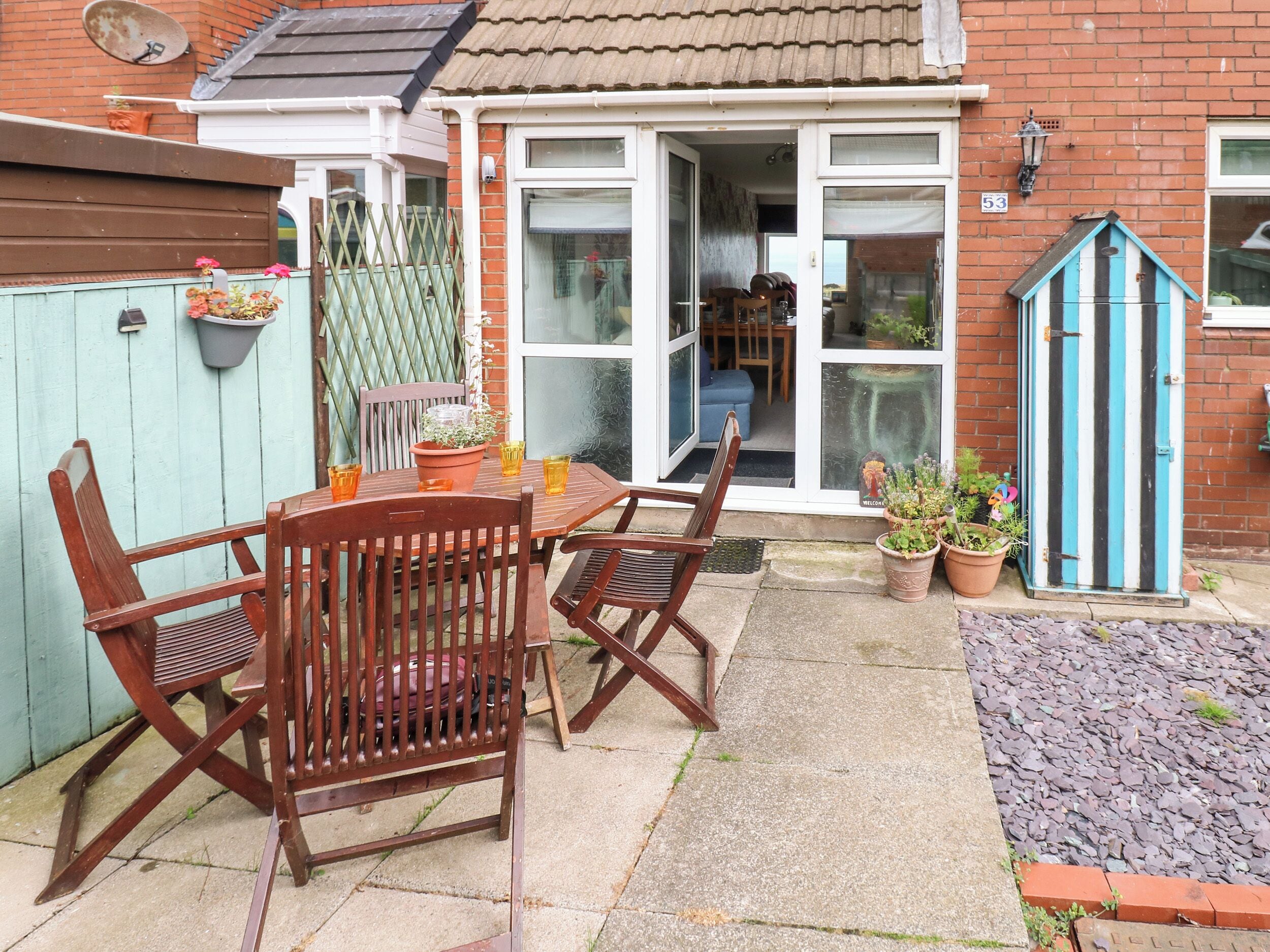 A patio with a wooden table and chairs, a blue gate, and potted plants.