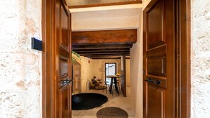 A hallway with wooden doors, a stone wall, and a small dining area with a table and chairs. - Oniros Residenza Vecchia  (Chania)