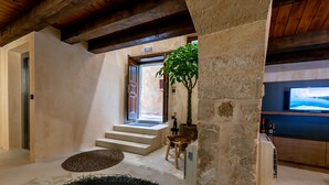A modern interior with a stone wall, a staircase leading to an outdoor area, a television, and a potted plant. - Oniros Residenza Vecchia  (Chania)