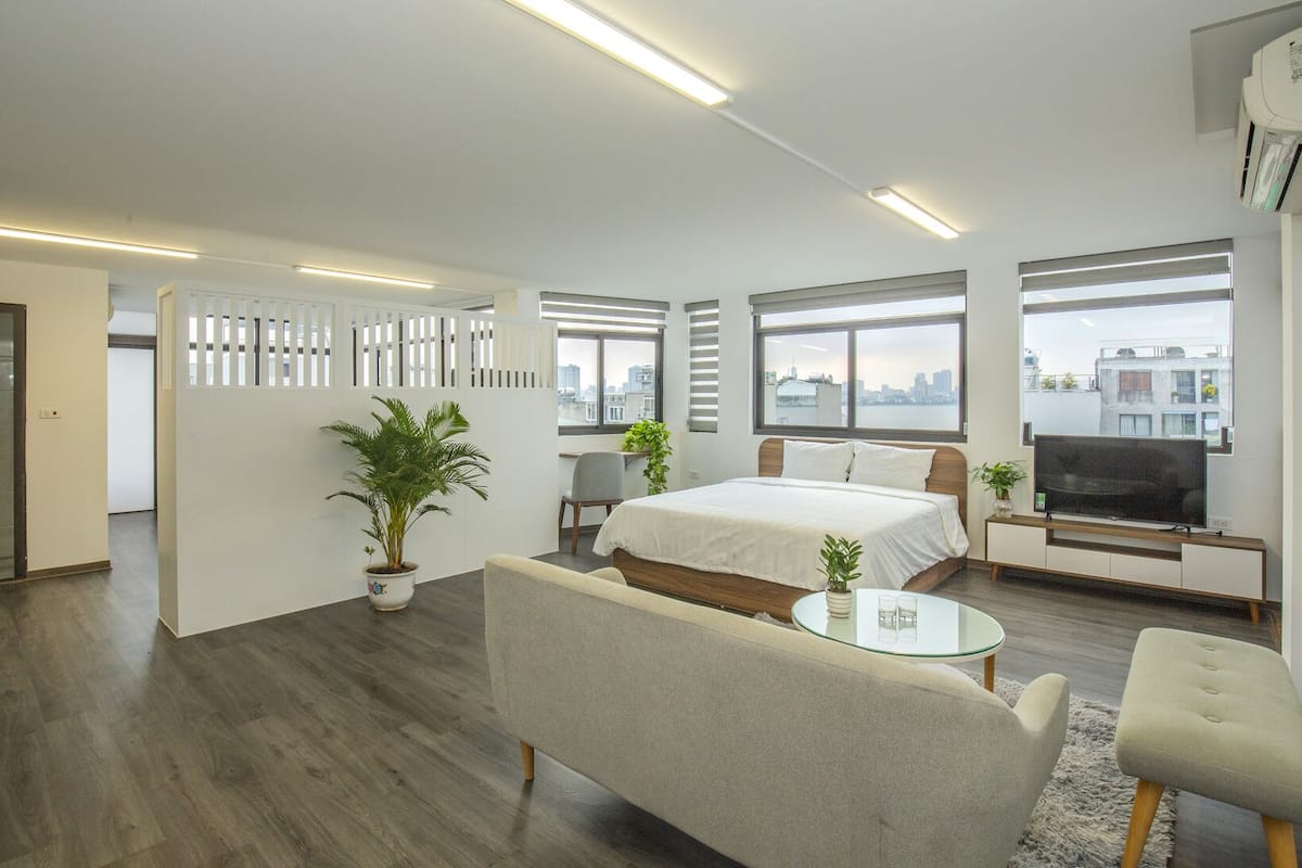 A modern hotel room with a bed, a TV, a sofa, and a glass coffee table.