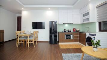 A modern kitchen with a dining area, a black refrigerator, a microwave, a washing machine, and a flat-screen TV.