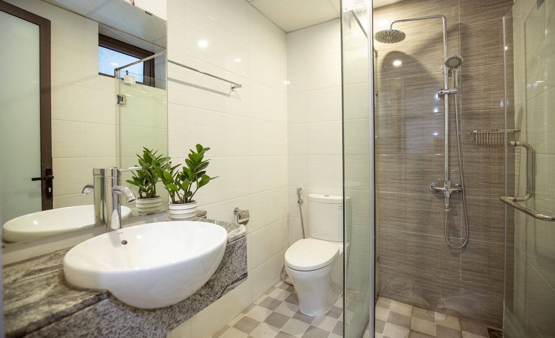 Un baño moderno con dos lavamanos, inodoro y ducha con cerramiento de vidrio.