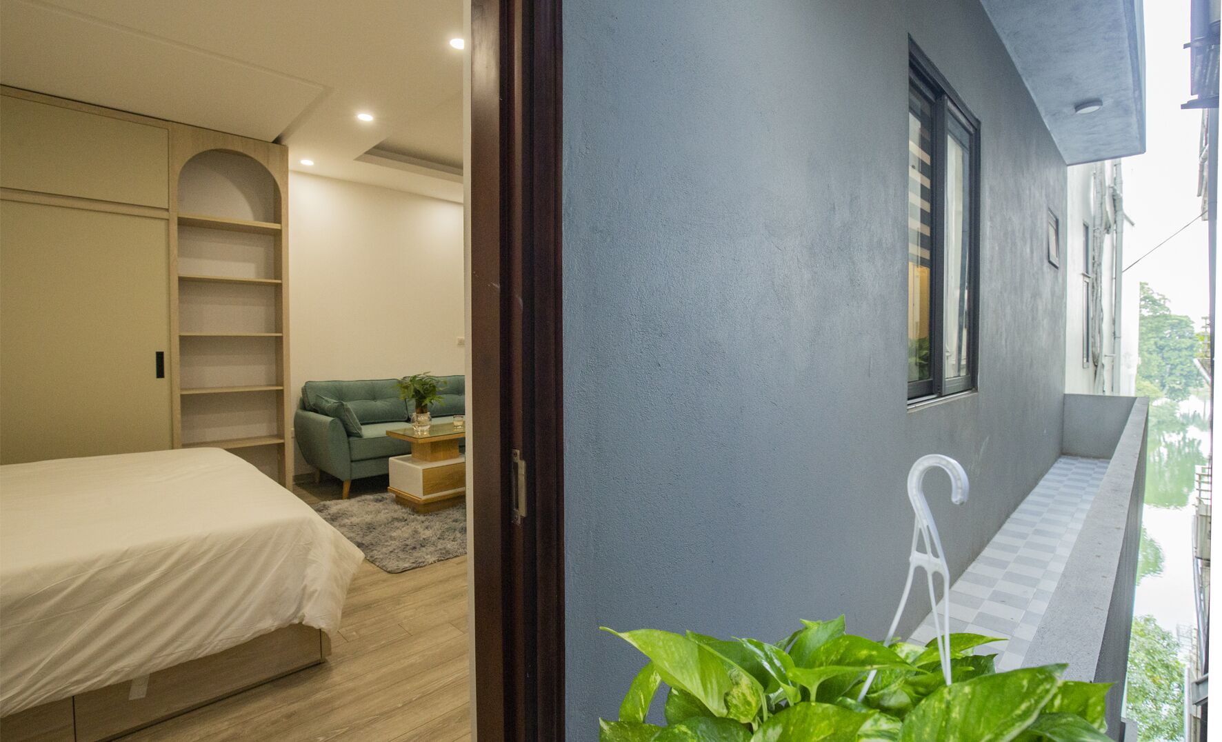 Un dormitorio con una cama, un sofá verde, una mesita con una planta y una ventana con persianas.