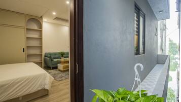 Un dormitorio con una cama, un sofá verde, una mesita con una planta y una ventana con persianas.