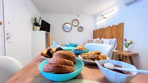 Un'area pranzo con tavolo in legno apparecchiato con diversi piatti, un letto con testiera in legno e una TV a muro.