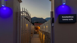 Ingresso recintato al Konstantinos Luxury suite, con muro in pietra e vista sulle montagne sullo sfondo.
