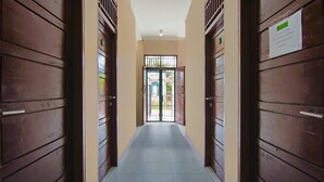 A corridor with wooden doors and a tiled floor, leading to a gate with a sign. - Hotel O Pondok Melati Syariah (Pekanbaru)