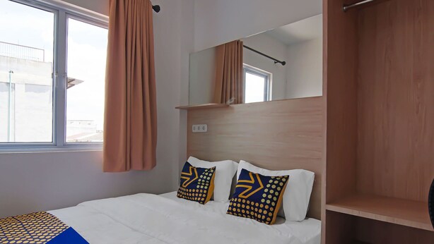 A hotel room with a bed, two pillows with geometric patterns, a window with curtains, a wooden headboard, and a mirror. - Hotel O Pondok Melati Syariah (Pekanbaru)