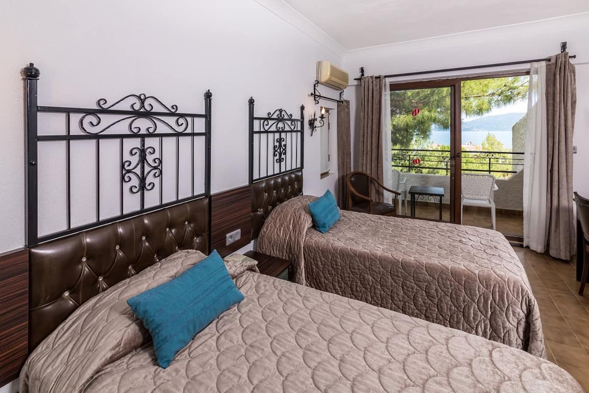 Habitación de hotel con dos camas, un balcón con mesa y sillas, y vistas al exterior.