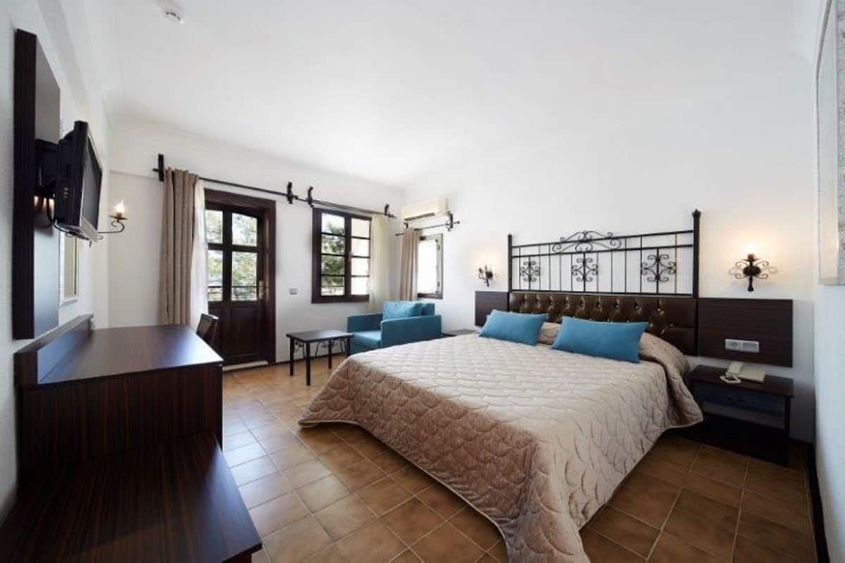 Un dormitorio con una cama grande, un escritorio, una silla y un televisor colocado en la pared.