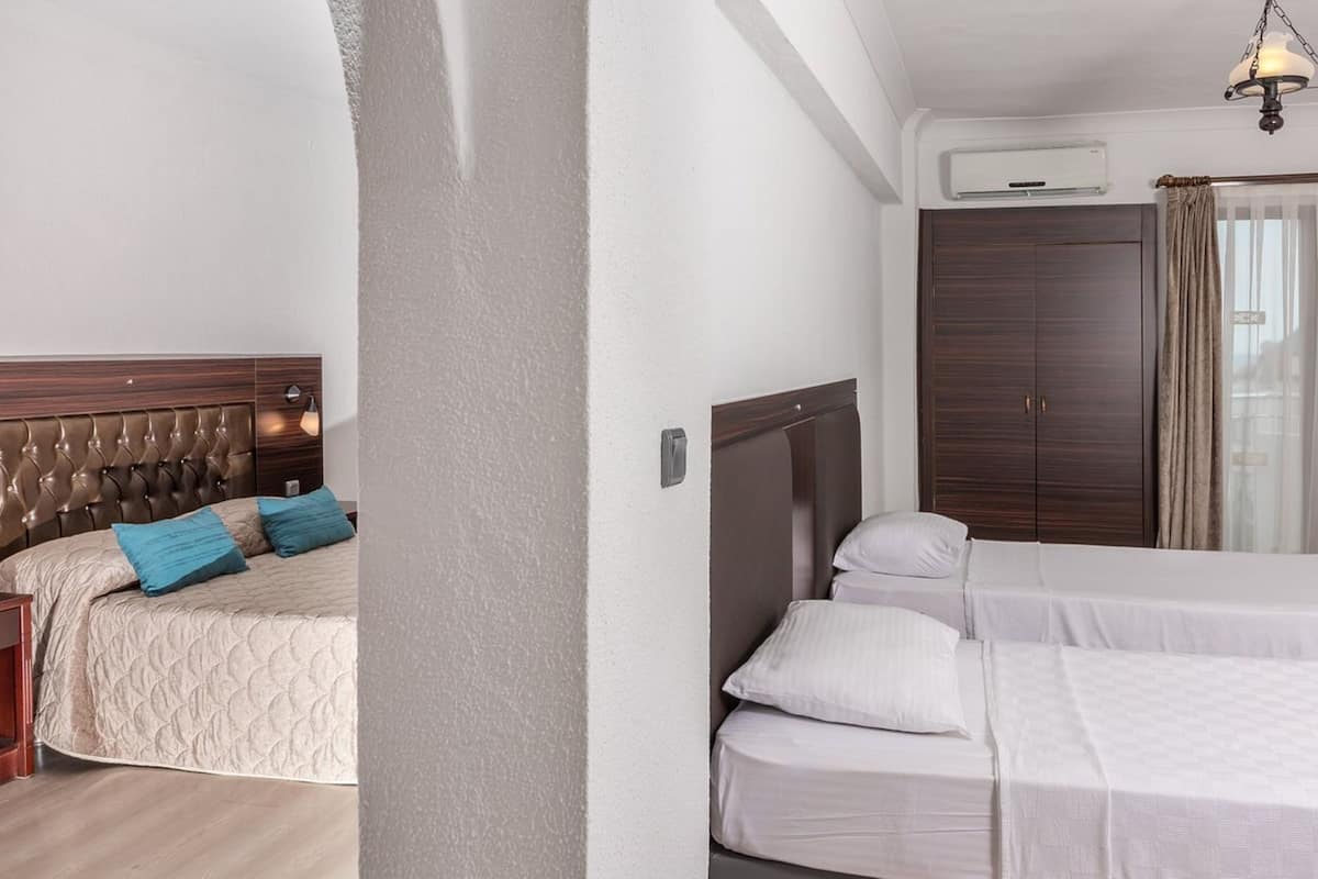 Habitación de hotel con una cama grande, una cama más pequeña, un armario, un aire acondicionado y una ventana con cortinas.