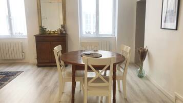Uma área de refeições com uma mesa de madeira redonda, cadeiras brancas, um espelho e um radiador.