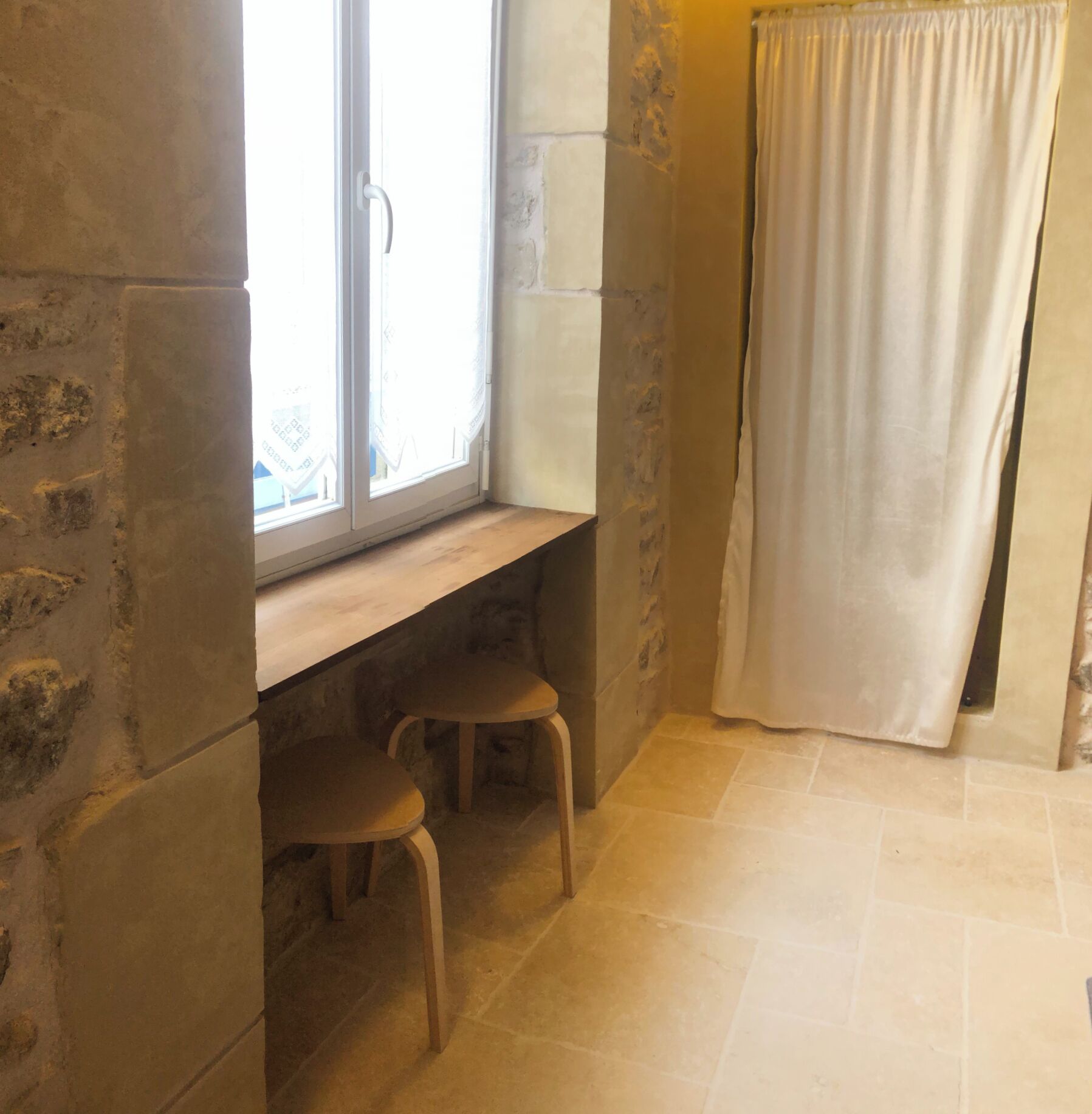 A bathroom with a window, two stools, and a shower curtain.