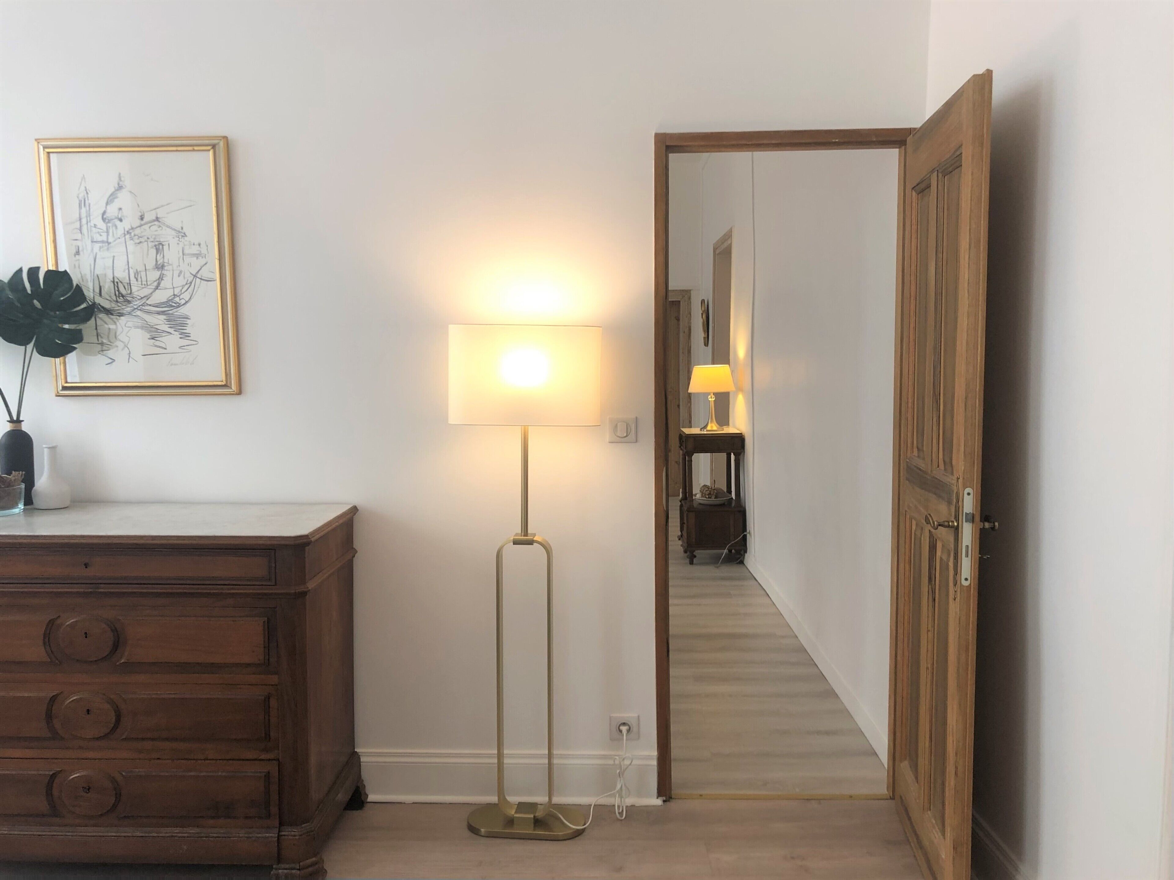 Ein Zimmer mit einem Holzkasten, einer Stehlampe und einem gerahmten Bild an der Wand.