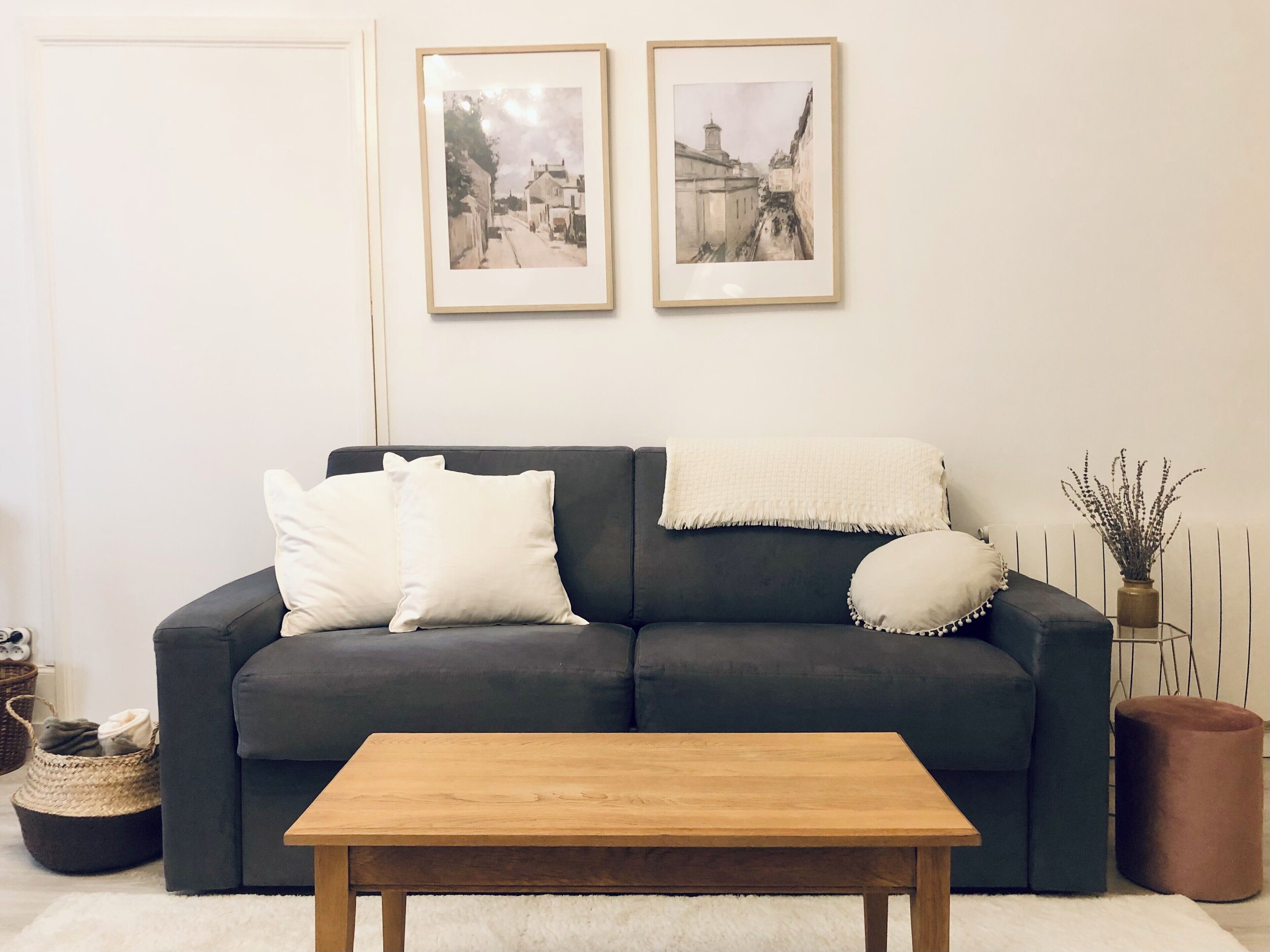 A living room with a dark grey sofa, two white pillows, a wooden coffee table, and two framed pictures on the wall.