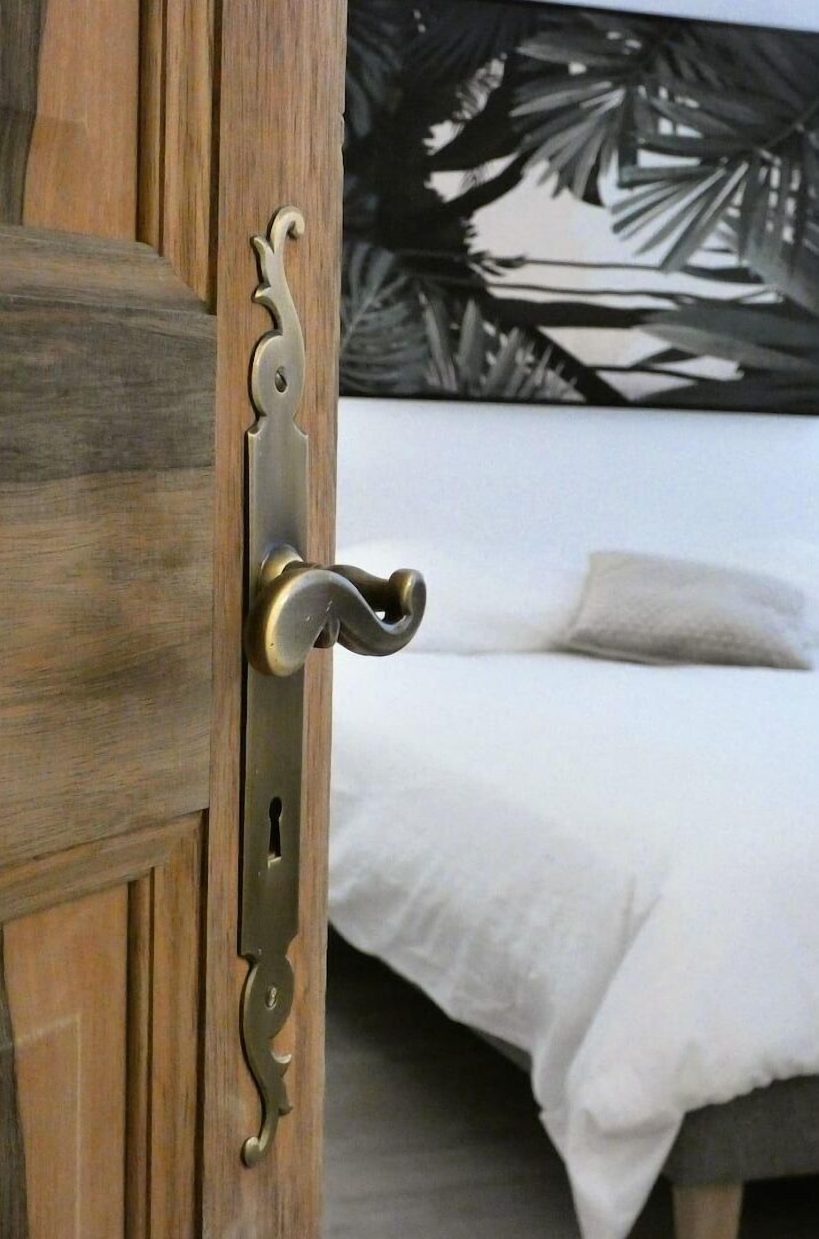 A wooden door with a brass handle and keyhole, leading to a bed with white bedding and a black and white abstract wall art.