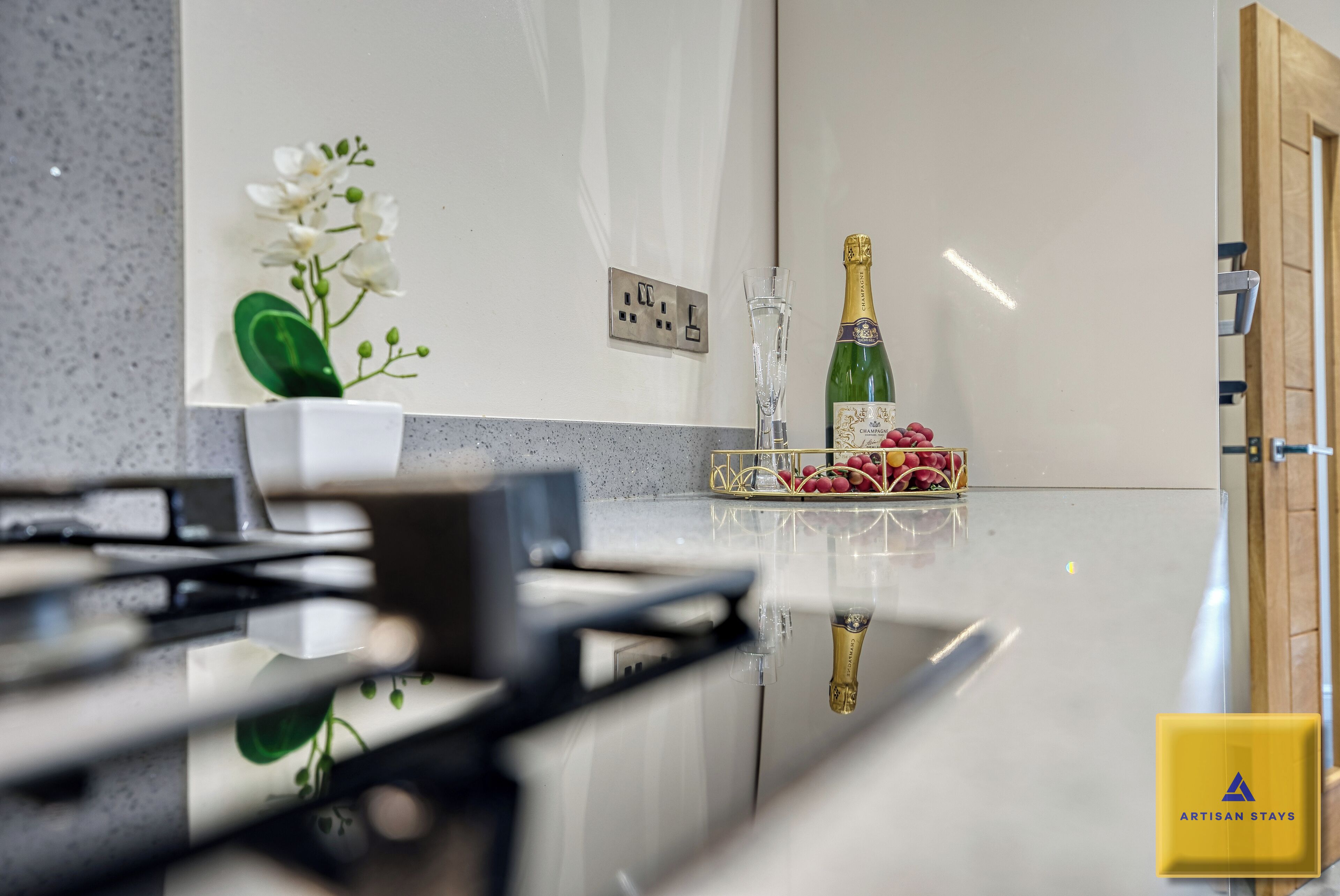 A modern kitchen with a marble countertop, a bottle of champagne, and a decorative orchid.