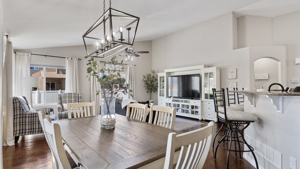 A dining area with a wooden table and chairs, a chandelier, and a TV in the background. - Welcome to your Entertainment Station! (Loveland)