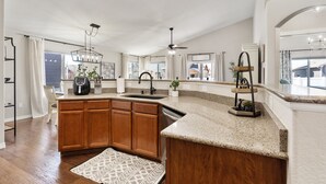 A modern kitchen with granite countertops, wooden cabinets, a built-in dishwasher, and a large island with a sink. - Welcome to your Entertainment Station! (Loveland)