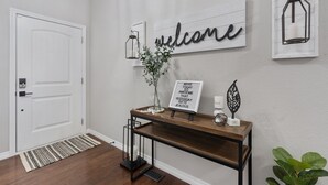 A hallway with a white door, a welcome sign, a lantern, a motivational sign, and a decorative leaf. - Welcome to your Entertainment Station! (Loveland)