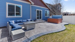 A blue house with a patio area featuring a sectional sofa, a glass-top coffee table, and a hot tub. - Welcome to your Entertainment Station! (Loveland)