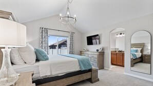 A bedroom with a bed, bedside table, lamp, dresser, mirror, and a view of the outside. - Welcome to your Entertainment Station! (Loveland)