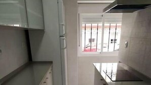 Eine schmale Küche mit grauen Schränken, einem weißen Kühlschrank und einer Spüle aus Edelstahl.