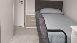 Ein kleiner, schmaler Raum mit einem Bett, einem Sessel und einer Tür zu einer Treppe.